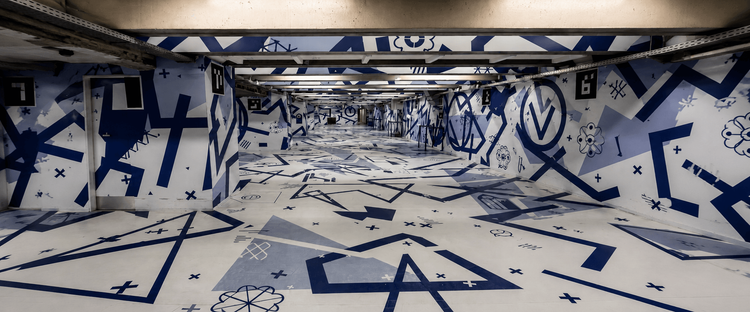 A corridor adorned with blue and white geometric patterns and symbols, featuring numbered doors and a clean, modern design